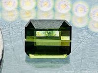 Emerald step-cut bright green tourmaline on reflective surface under ring light