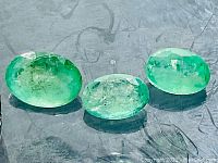 Close-up photo of three oval natural emeralds showing color and clarity details.