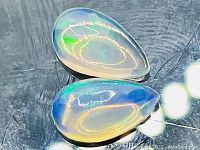 Two pear-shaped cabochon cut Ethiopian opals on reflective background, showing color play