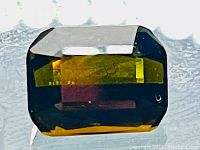 Close-up image of the olive green rectangular scissor cut tourmaline gemstone against a light background, showing facets and rich color.