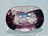 Front-facing close-up of oval cut spinel on reflective surface