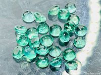 Twenty-five mixed sizes round faceted green emerald gemstones on reflective surface