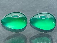 Two pear-shaped vivid green onyx cabochon gemstones, shown side by side on dark reflective surface, glossy finish visible.