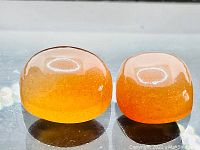 Two cabochon sunstones placed side-by-side showing their rounded cushion shape, translucent orange color, and glittering gold inclusions.