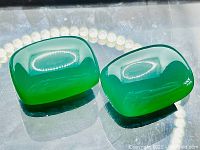 Two vivid green onyx cabochon cut stones side by side on a reflective surface showing color and cut clearly.
