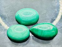 Three polished malachite stones displayed together showing unique colors and patterns with glossy finish.