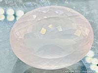 Close-up photo of oval cut rose quartz gemstone showing facets and pale pink color.