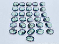 Top view of 36 calibrated oval synthetic Mystic Topaz gemstones displaying iridescent colors including green, blue, and purple hues.