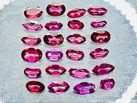 Loose pink to purple rhodolite garnet gemstones arranged in rows, showing mixed oval and marquise cuts and varying sizes.
