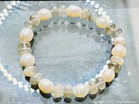 Front view of the stretchy bracelet showing alternating freshwater pearl and moonstone beads on a reflective surface.
