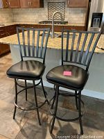 Pair of two iron swivel bar stools with black cushioned seats, vertical slat backrests, placed in a kitchen area.