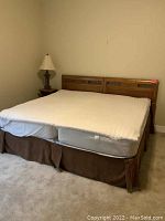 Set of two twin wooden beds put together as a king bed, viewed from the side showing white mattress pad and brown bed skirt