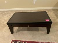 Dark wood rectangular coffee table with drawer closed, showing the front and top surfaces clearly on carpeted floor.