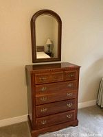 Front view of wooden dresser with attached arched mirror showing five drawers and brass-tone handles.