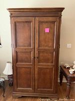 Full front view of the wooden entertainment center showing closed double paneled doors with round knobs, classic brown finish, decorative crown molding on top and base.