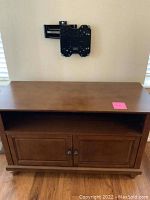 Front view of small wooden entertainment center under a wall-mounted TV bracket, showing open shelf and double cabinet doors.