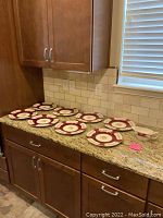 Eight ivory Steubenville dinner plates with maroon and gold border and floral details arranged on kitchen counter
