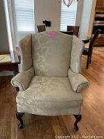 Front view of beige upholstered wingback armchair with floral pattern, showing seat cushion, rolled arms, and winged backrest.