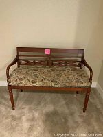 Front view of wooden bench with carved backrest and floral patterned upholstered seat, showing overall condition and design.