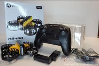 Photo shows Holy Stone HS450 mini drone in yellow and black with propeller guards, black controller, spare battery, spare propellers sealed in plastic, and the original box.