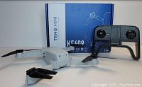 Teng Mini KF 609 drone in white with foldable arms and black propellers, remote controller, and original blue and white box with branding.