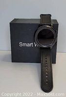 Black smart watch with a round face and black leather strap placed in front of a black box labeled 'Smart Watch'.