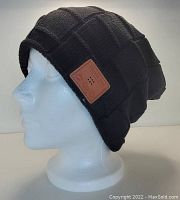 Black quilted Bluetooth knit hat displayed on a white mannequin head, showing its textured pattern and leather-like Bluetooth control patch on the side.