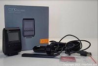 Photo showing Apeman C370 dash camera, packaging box, car charger, USB cable, mounting stick, and user manual all placed on a white surface.