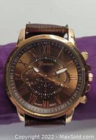 Geneva wristwatch with brown leather band and gold-tone case. Watch face shows Roman numerals and three subdials. Brown textured leather strap.