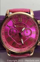 Hot pink Geneva wristwatch with gold-tone Roman numerals and leather band, front close-up of watch face.