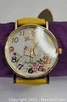 Front view of Geneva Platinum yellow and gold floral faced wristwatch with leather band, showing dial with floral pattern and gold-tone numerals and hands.