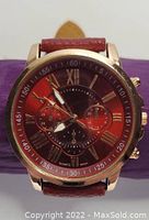 Front view of gold-tone analog quartz watch with red dial, three subdials, Roman numerals, and red leather strap.
