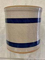 Front view of cylindrical beige stoneware crock with two blue horizontal bands showing smooth glazed surface.