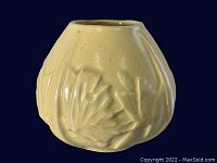 Yellow Art Deco style vase placed on clear stand against black background, showing embossed leaf details