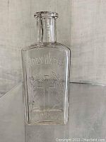 Front view of clear glass antique holy water bottle showing embossed 'HOLY WATER' text and cross with laurel design.