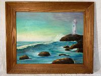 Front view of the framed folk painting depicting a coastal scene with lighthouse, rocks, and ocean waves.