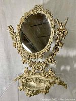 Front view of antique cast iron mirror showing oval mirror with intricate floral and bird decorations and decorative cast base.