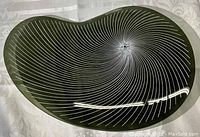 Top view of dark tinted kidney-shaped glass tray showing spiral linear pattern and smooth surface.