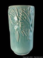 Front view of light blue cylindrical ceramic vase embossed with a butterfly and foliage design against a black background.