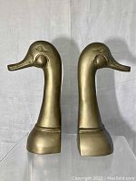 Front view of the pair of brass duck head bookends showing their detailed facial sculpting and polished brass finish.