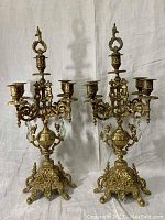 Pair of large ornate brass candelabras, one with 4 candle holders and the other with 3, standing side by side.