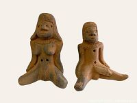 Front view of pair of seated male and female clay fertility flutes showing detailed facial features, hair, and anatomical emphasis.