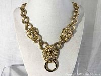 Front view of gold-tone lion head necklace on display bust, showing lion heads and central ring detail.