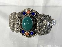 Front view of the bracelet highlighting the central large green stone with blue and orange smaller stones and dragon motifs on a silver-toned metal band.
