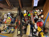 Wide view showing assorted automotive supplies including two car jacks, many bottles and cans of automotive fluids, cleaning supplies, and accessories arrayed on a garage floor.