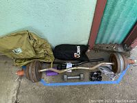 Rusty metal barbell with attached weight plates, gray 5 pound dumbbells, and purple 1 pound hand weights with nylon backpack in background.