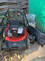 Front view of the red and black Yard Machines lawn mower with attached grass catcher and engine oil beside it.