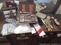 Overview of vintage leather travel case with nail care tools, assorted grooming brushes, hand mirrors, shoe horns, and bead strands arranged on wooden dresser