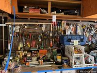 Wide view of workbench with pegboard displaying various handtools including screwdrivers, wrenches, levels, tape, nails, and toolboxes organized on shelves and hooks.