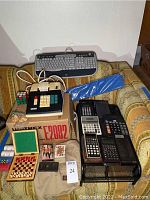 Photo showing two vintage HP scientific calculators, HP keyboard, Unitrex adding machine in original box, Rubik's cube, poker chips, and board games